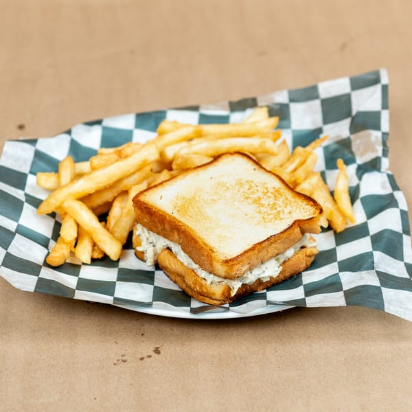 Toasted sandwich with creamy filling and golden french fries on checkered paper.