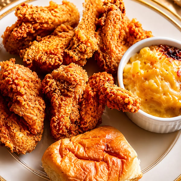 Crispy fried chicken pieces, a side of baked mac and cheese, and a dinner roll on a white plate.