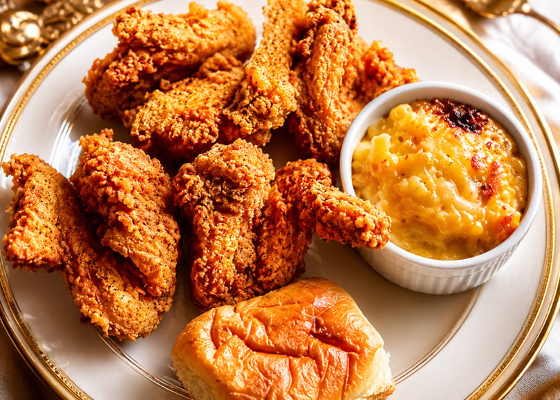 Crispy fried chicken pieces, a side of baked mac and cheese, and a dinner roll on a white plate.