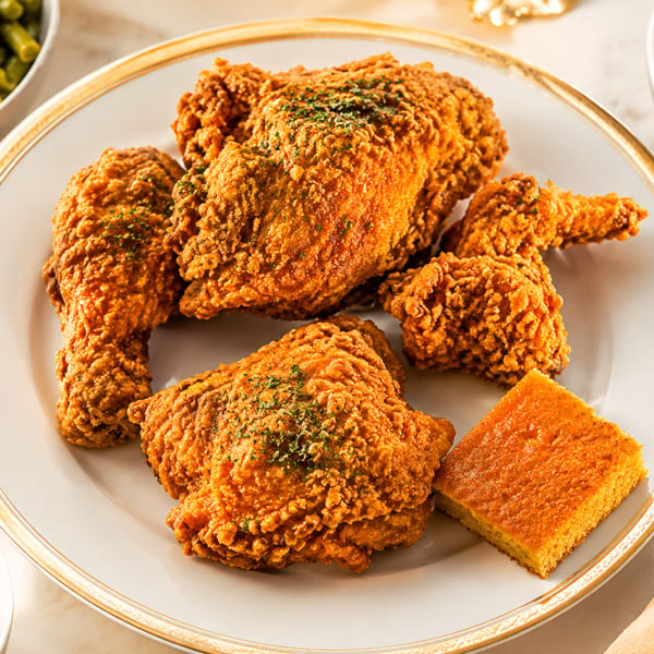 Golden fried chicken pieces and cornbread on a white plate, surrounded by side dishes.