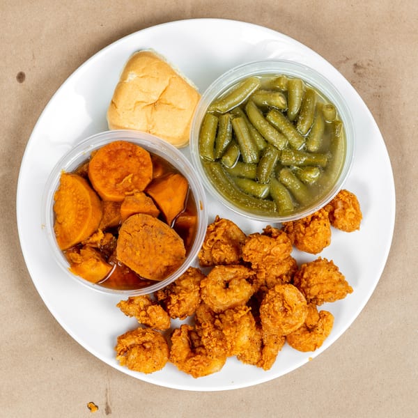 Fried shrimp, green beans, candied yams, and a dinner roll on a white plate.