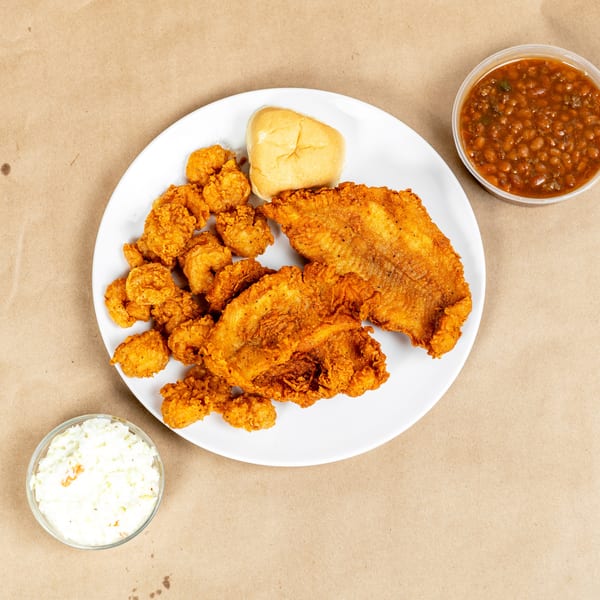 Fried fish and shrimp with a bun, baked beans, and coleslaw on a brown surface.